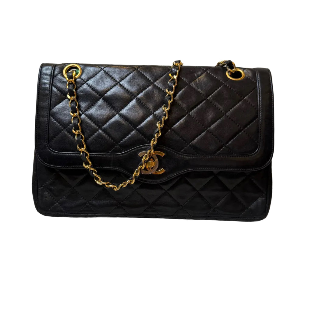 Black quilted handbag with gold chain and clasp on a patterned surface